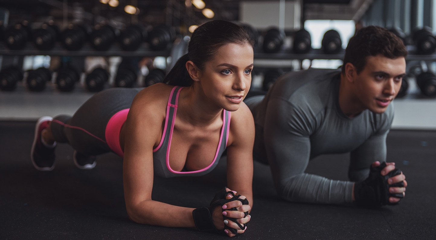 Attractive young muscular man and woman doing plank exercise while working out in gym